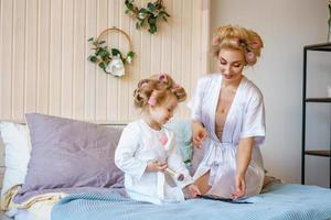 happy mom and daughter make a make-up sitting on the bed in the bedroom photo