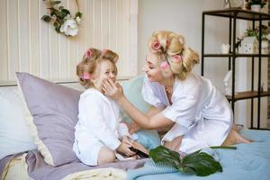 madre e hija en rulos y bata en la cama foto