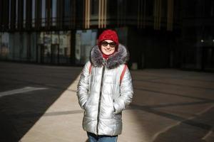 Happy young woman in winter jacket with backpack near building photo