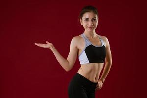 Young woman in sportswear on a red background shows with her hand to the side photo