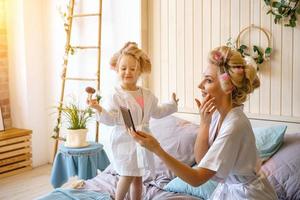 happy mom and daughter make a make-up sitting on the bed in the bedroom photo