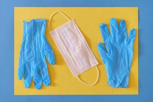 White medical mask with blue latex gloves close-up on yellow background, protection concept photo