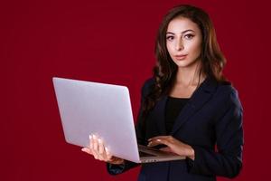 Beautiful young business woman with laptop on red background photo