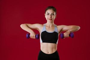 Sporty woman with dumbbells in hand on red background photo