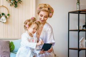 mom and daughter in curlers , make a make-up to each other, a happy family photo