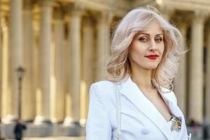 retrato de una linda mujer rubia con una chaqueta blanca en la calle en un día soleado foto