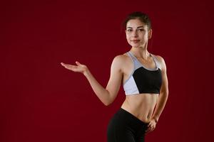 Young woman in sportswear on a red background shows with her hand to the side photo