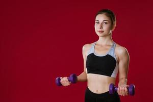 Sporty woman with dumbbells in hand on red background photo