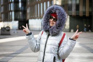 mujer joven feliz en chaqueta de invierno con mochila cerca del edificio foto