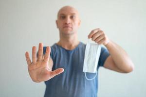 A bald man holds a medical mask in his hands, his other hand held out in protest photo
