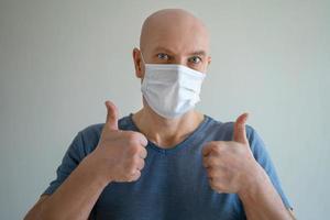 retrato de un hombre calvo con una máscara médica, muestra un gesto de mano como un dedo hacia arriba foto