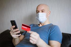 Bald man in protective mask with phone and credit card in hand photo