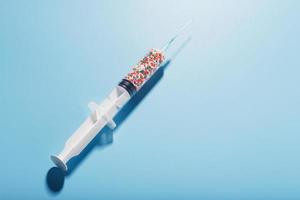 A syringe with colored balls on a blue background, free space. Top view. photo