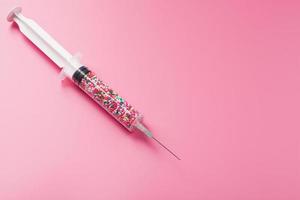 Medical Syringe filled with colorful balloons on a pink background with free space. photo