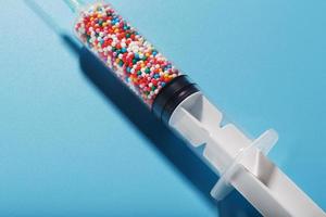 A syringe with colored balls on a blue background, free space. Top view. photo