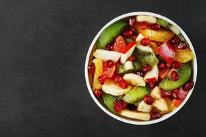 taza de ensalada de fruta fresca hecha de frutas jugosas sobre un fondo negro. foto
