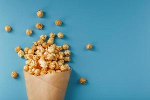 Popcorn in caramel glaze in a paper envelope on a blue background. photo