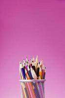 Pencils of different colors in a glass on a pink background. photo