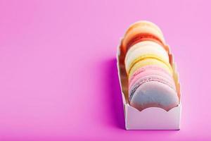 Colorful French macarons cookies in a package on a pink background. photo