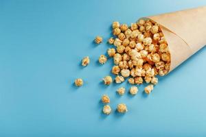 Popcorn in caramel glaze in a paper envelope on a blue background. photo