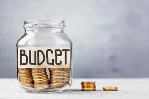 A glass jar with money and the inscription BUDGET, with a sticker with free space for text, on a gray background. photo