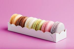 Colorful French macarons cookies in a package on a pink background. photo