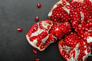 The opened Fruits of a ripe open pomegranate lie on a black textural background. photo