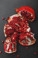 The opened Fruits of a ripe open pomegranate lie on a black textural background. photo