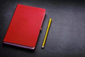 Red Notepad with a marker on a black background, top view. photo