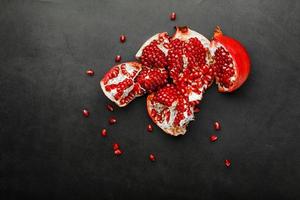 The opened Fruits of a ripe open pomegranate lie on a black textural background. photo