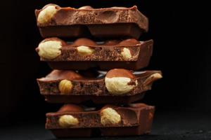 Chocolate with hazelnut in the form of a tower on a dark background. Pieces of milk chocolate with nuts. photo