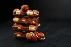 Chocolate with hazelnuts in the form of a tower on a dark background, surrounded by nuts in the shell and peeled. photo