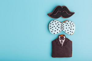 Glazed gingerbread in the form of a mustache, butterfly and tuxedo, men's set on a blue background. Handmade cookies. photo