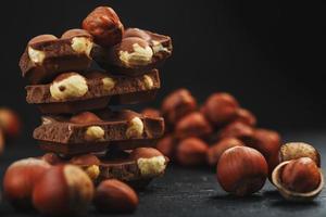 Chocolate with hazelnuts in the form of a tower on a dark background, surrounded by nuts in the shell and peeled. photo