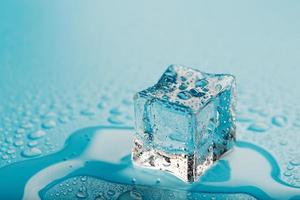 cubo de hielo con gotas de agua sobre un fondo azul. El hielo se está derritiendo. foto