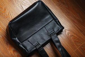 Handmade black leather bag on a wooden background, made of natural material. photo