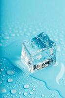 Ice cube with water drops on a blue background. The ice is melting. photo