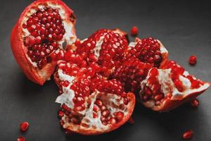 The opened Fruits of a ripe open pomegranate lie on a black textural background. photo