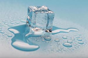 Ice cube with water drops on a blue background. The ice is melting. photo