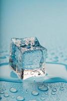 Ice cube with water drops on a blue background. The ice is melting. photo