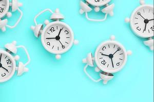 A pattern of many white classic alarm clocks in the form of a pattern on a blue background. Top view with a copy of the space, flat lay. photo