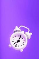 White retro style alarm clock in levitation isolated on purple background. photo