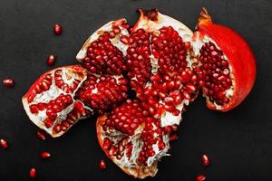 The opened Fruits of a ripe open pomegranate lie on a black textural background. photo