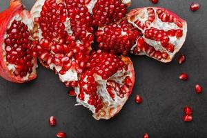 The opened Fruits of a ripe open pomegranate lie on a black textural background. photo