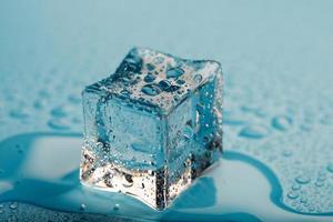 cubo de hielo con gotas de agua sobre un fondo azul. El hielo se está derritiendo. foto