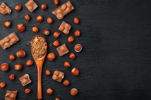 chocolate con avellanas y una cuchara de madera con cacao sobre un fondo oscuro, rodeado de nueces con cáscara y peladas. foto