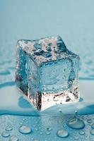 Ice cube with water drops on a blue background. The ice is melting. photo