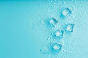 cubos de hielo con gotas de agua esparcidas sobre un fondo azul, vista superior. foto