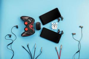 A predatory monster-fish from gadgets eats a white alarm clock on a blue background. The creature in the form of various smartphone gadgets, gamepad and headphones devours time. photo