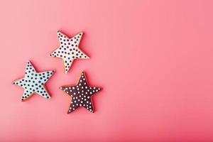 A close-up of three homemade glazed gingerbread cookies is made in the form of stars on a pink background. Handmade cookies. photo